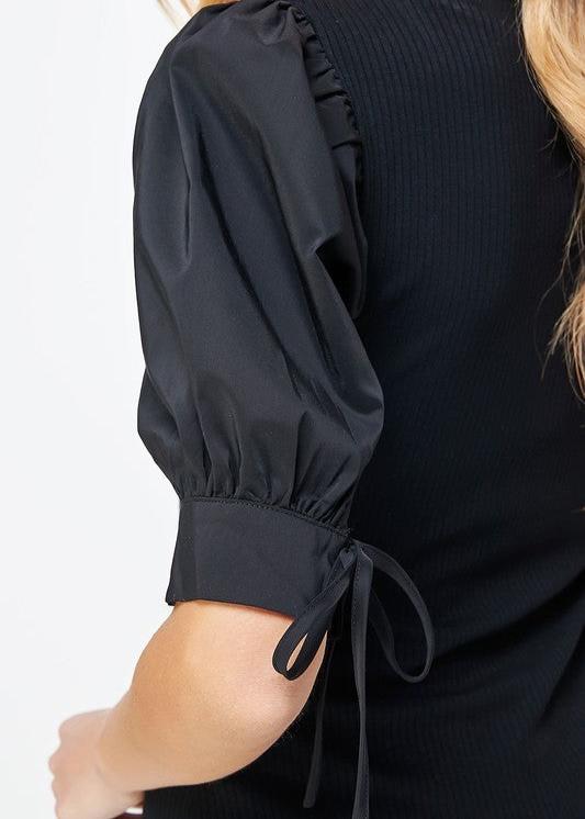 Black poplin sleeve knit top. This style features bodice in ribbed knit, a classic V neckline, and & poplin short sleeves with cuff and tie detail.