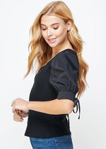 Load image into Gallery viewer, Black poplin sleeve knit top. This style features bodice in ribbed knit, a classic V neckline, and &amp; poplin short sleeves with cuff and tie detail.
