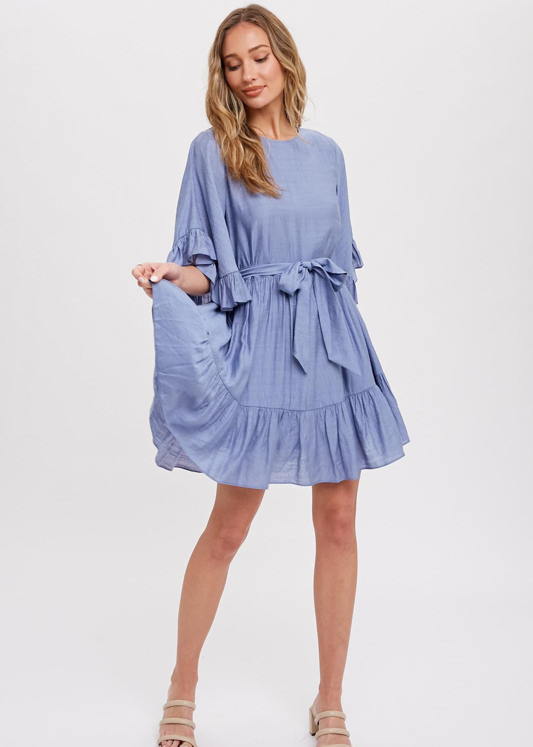 Chambray mini dress features a round neck, along with flounce sleeves that have a loose and flowy appearance. It also has a self-tie belt at the waist, which allows for a customizable and fitted look. The bottom of the garment is finished with ruffles and frill detailing, adding a decorative touch and creating a playful and feminine style.