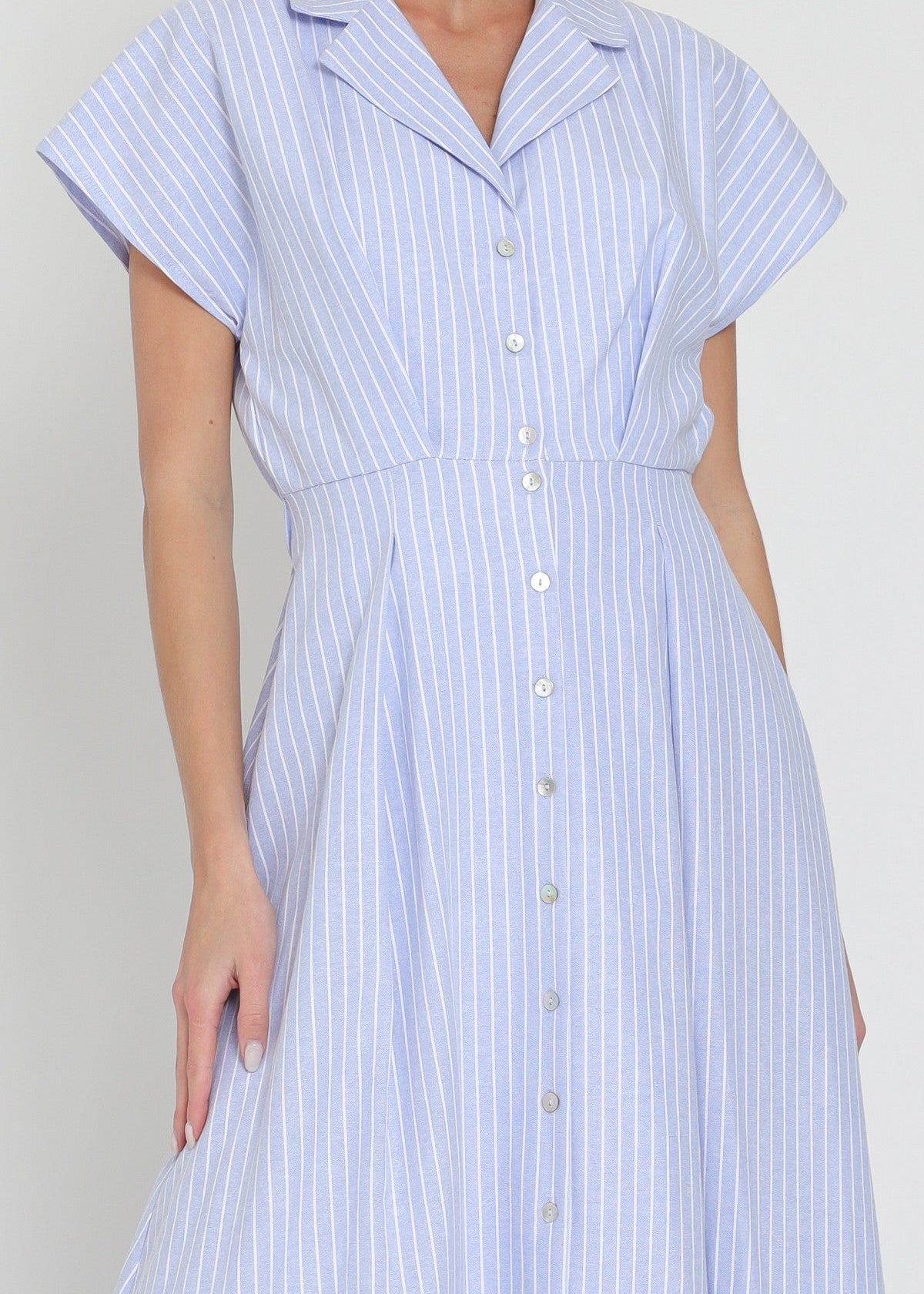 Woman wearing a light blue and white striped dress against a plain background