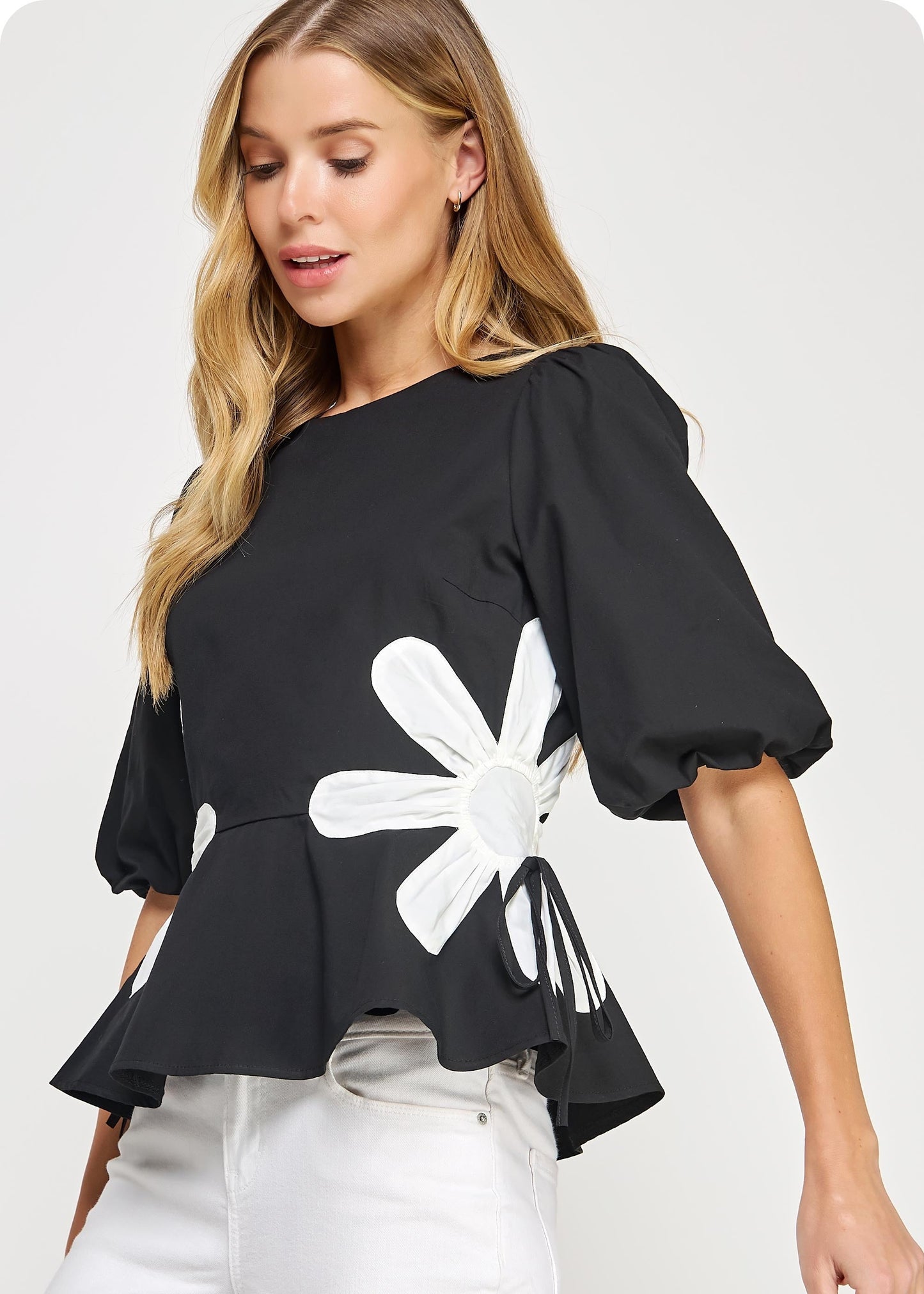 Black &amp; off white flower detail color blocked blouse in cotton poplin fabric. This style features half puff sleeves, shirred shoulders, feminine patchwork flower detail at sides with tie detail, round neck and cinched waist with peplum hem.