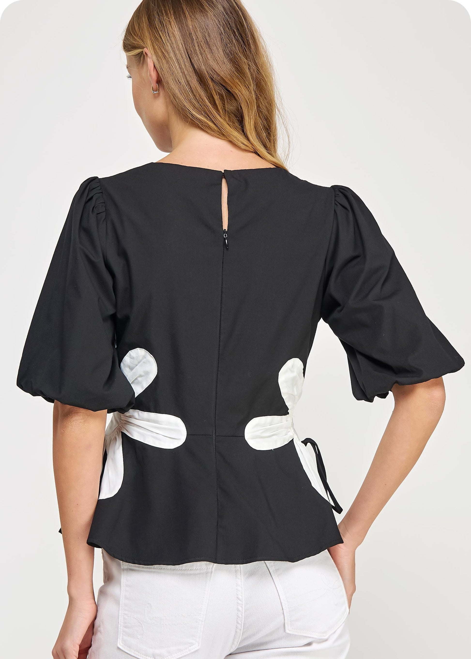 Black &amp; off white flower detail color blocked blouse in cotton poplin fabric. This style features half puff sleeves, shirred shoulders, feminine patchwork flower detail at sides with tie detail, round neck and cinched waist with peplum hem.
