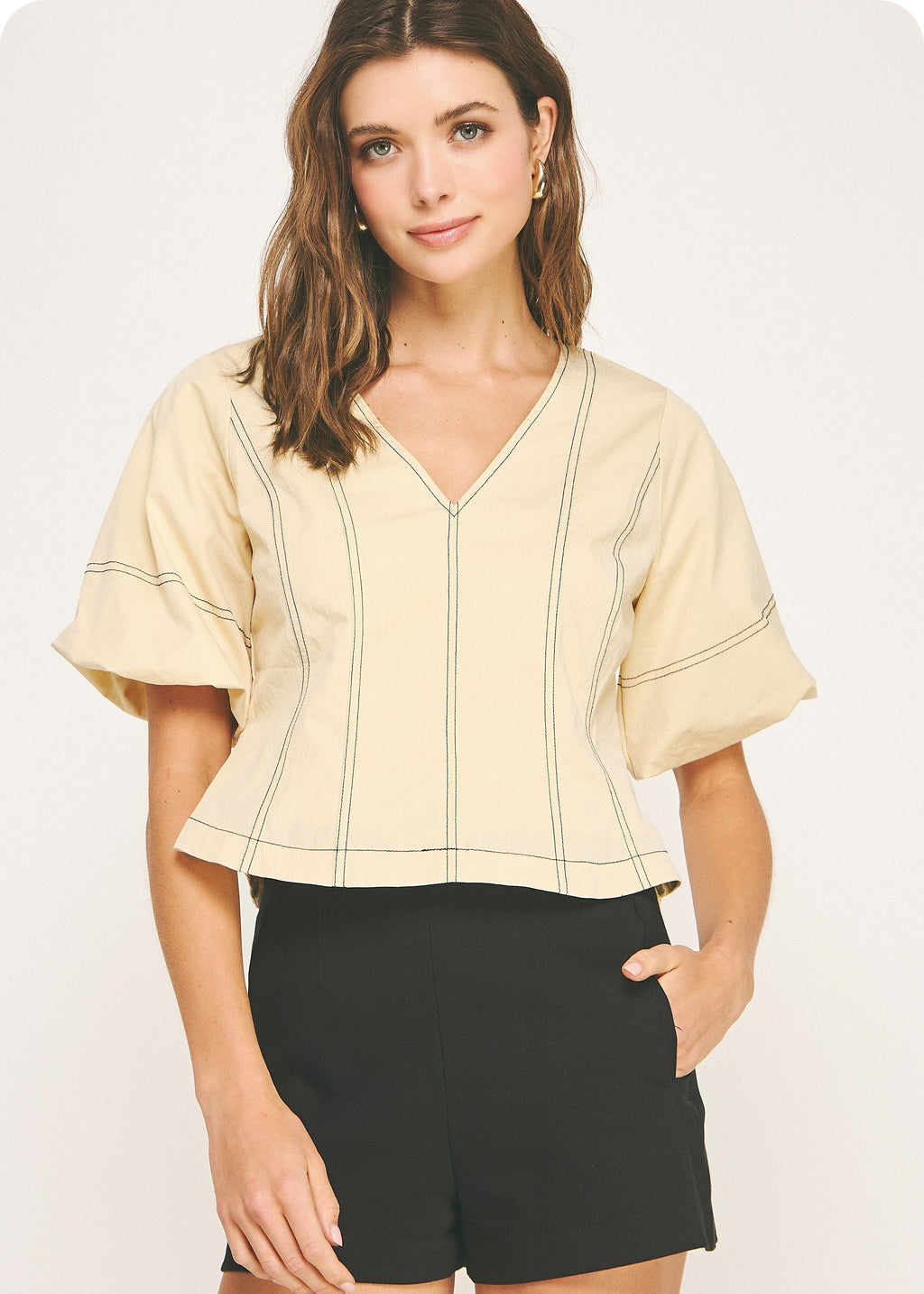 Butter and black top stitch top in stretch cotton blend fabric. This blouse features a V neckline, puff short sleeves, a hidden side zipper closure, top-stitch detail throughout, and tucked waist with flare hem.