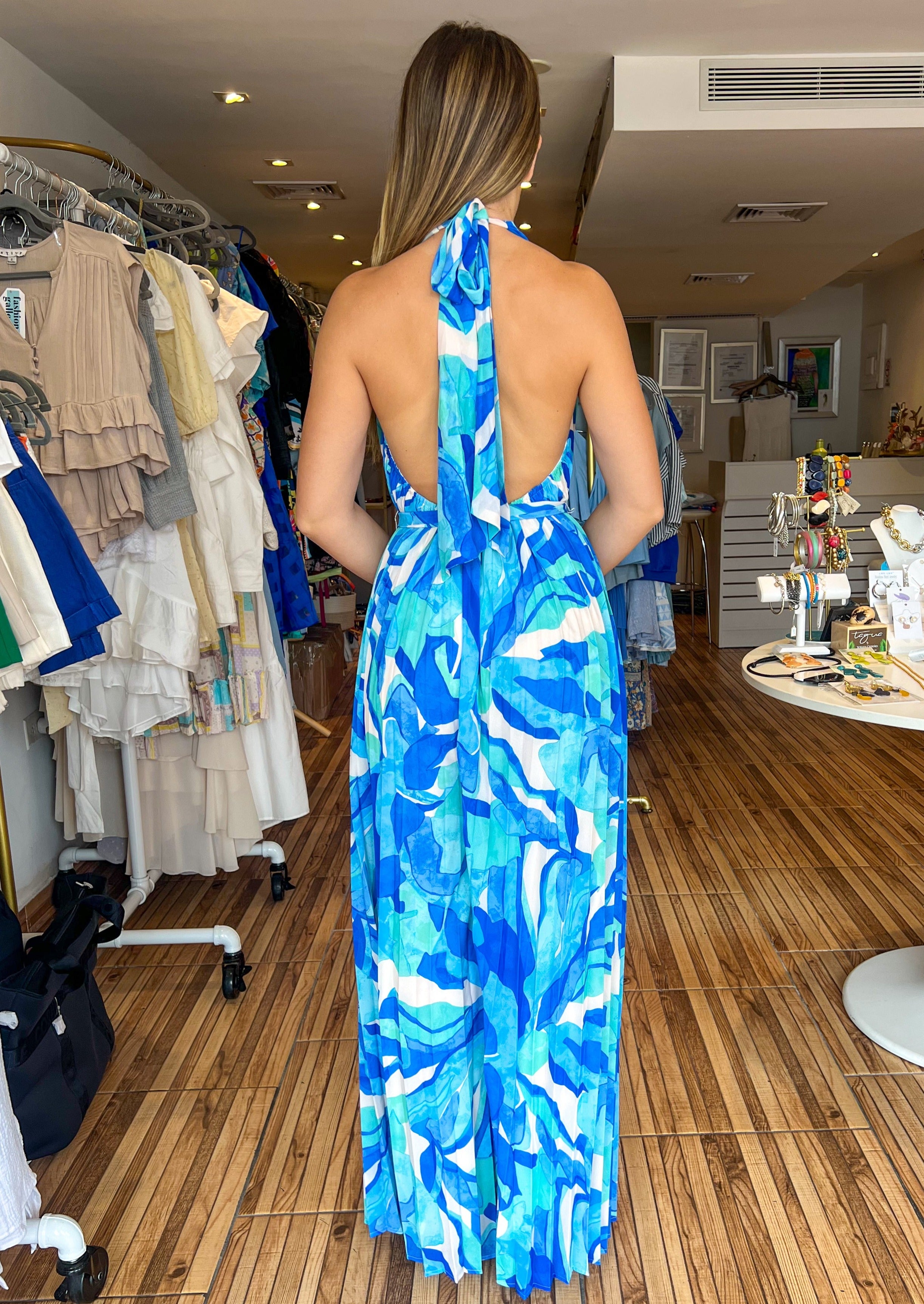 Blue printed woven jumpsuit featuring plunging V halter neckline, sleeveless, wide leg, self sash tie and bare back.