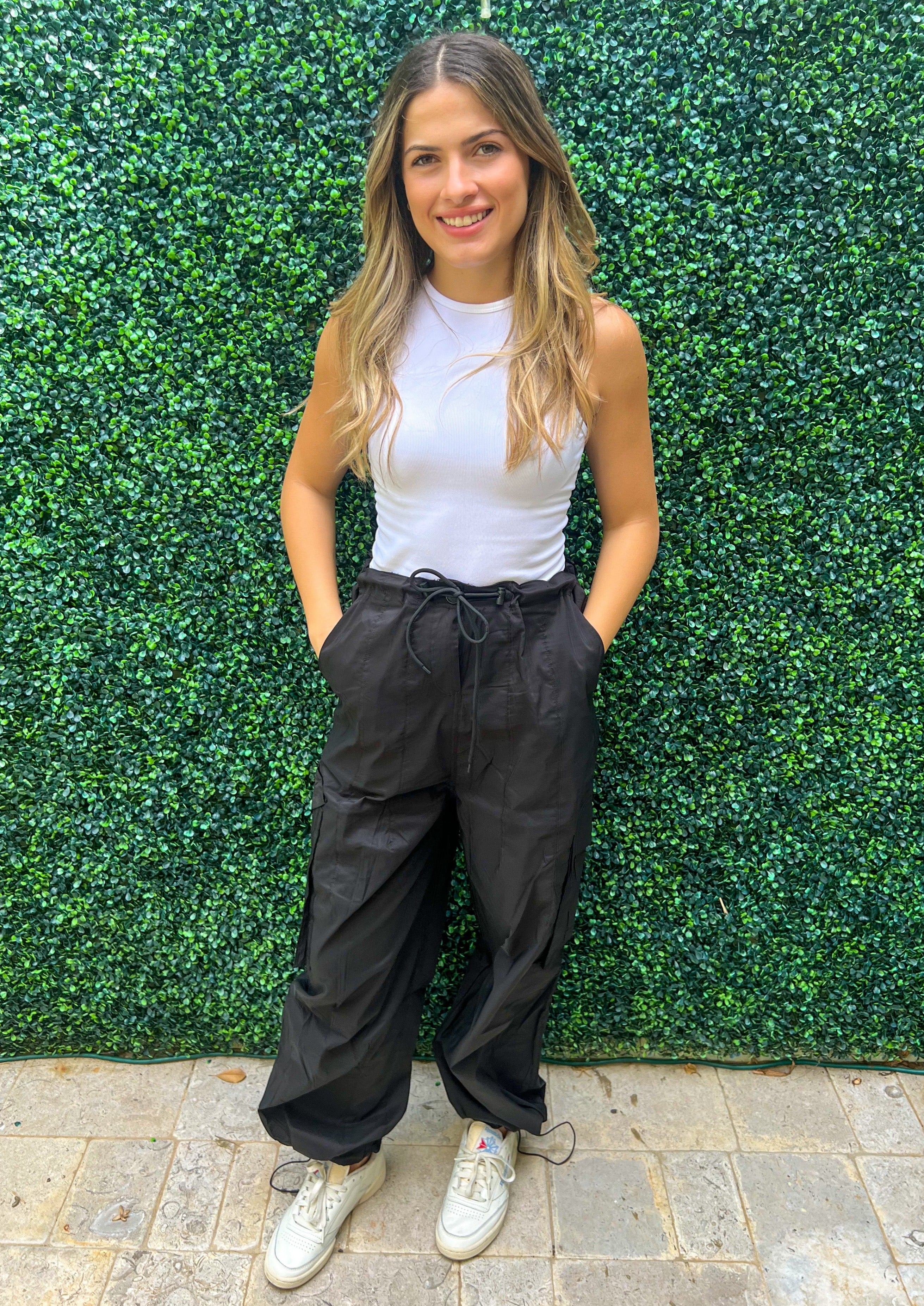 High waisted elastic waist band black cargo pants with pockets and side pockets. Bottom of the pants feature elastic so they can be worn loose or adjusted.