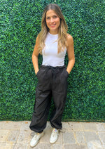 Load image into Gallery viewer, High waisted elastic waist band black cargo pants with pockets and side pockets. Bottom of the pants feature elastic so they can be worn loose or adjusted.
