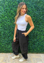 Load image into Gallery viewer, High waisted elastic waist band black cargo pants with pockets and side pockets. Bottom of the pants feature elastic so they can be worn loose or adjusted.
