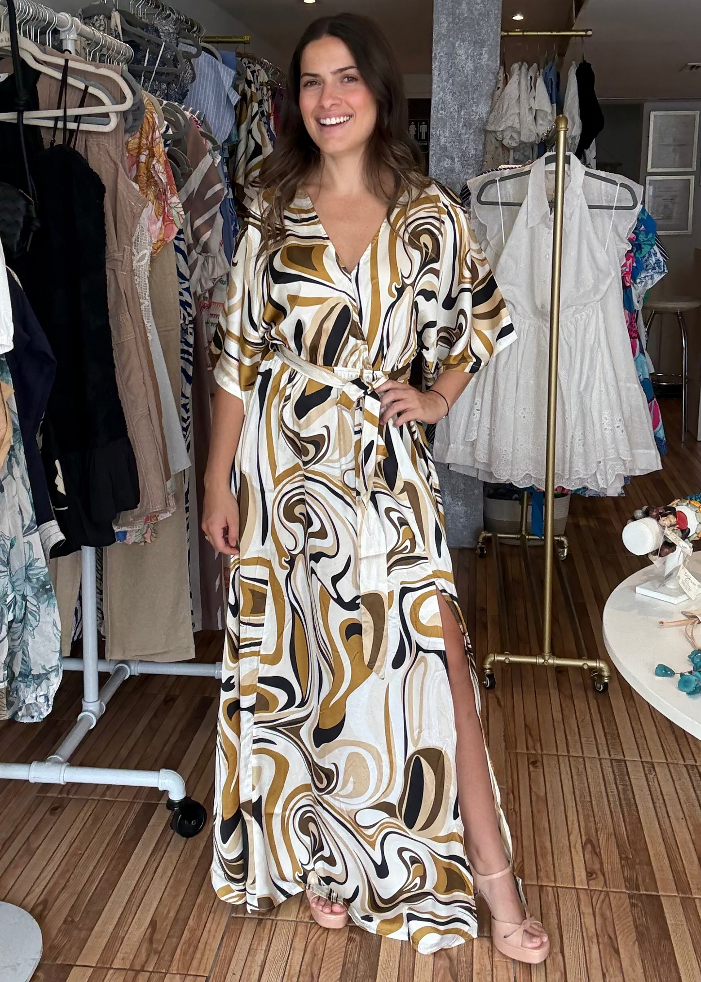 Woman in a patterned dress standing in a clothing store with racks of clothes in the background.