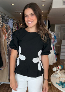 Woman wearing a black top with white floral patterns in a clothing store.