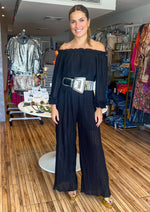 Load image into Gallery viewer, Black off shoulder pleated jumpsuit in chiffon fabric. Featuring elasticated off shoulder neck line, wide leg pants, lining, elastic at waist, long sleeves with ruffle lettuce edge detailing, and removable cinching waist tie, this jumpsuit is completely pleated and has a relaxed fit.
