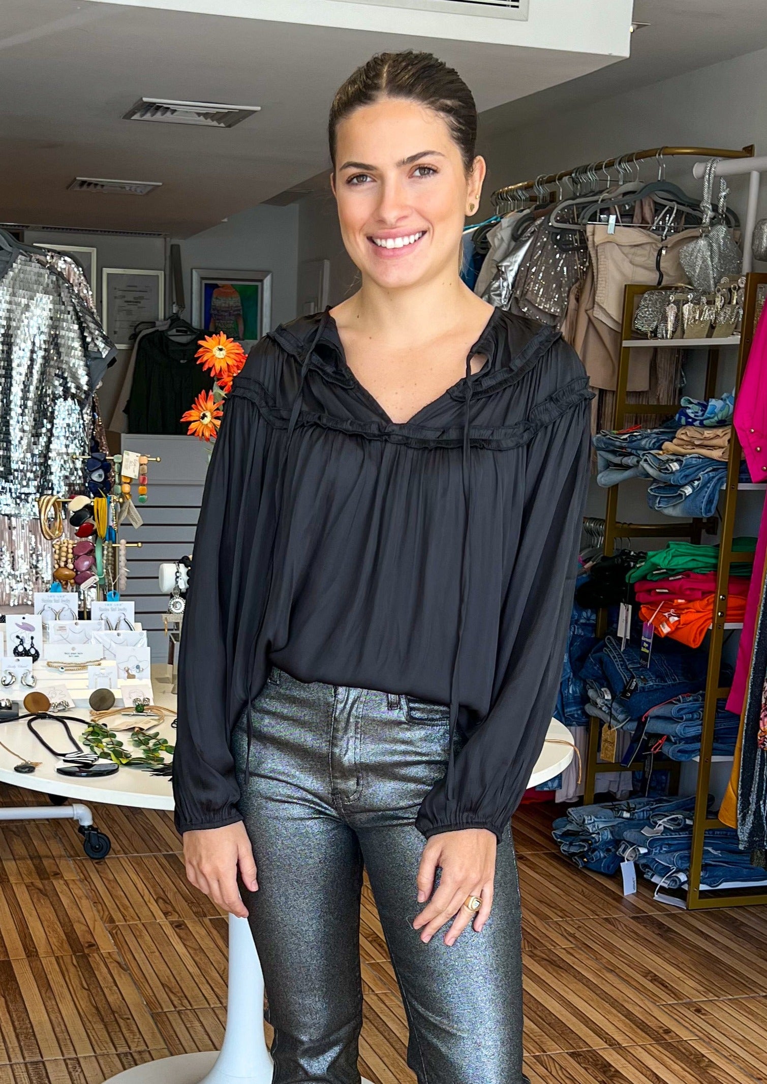 Ruffled blouse in washed satin fabric. This style features a classic V neck with tie closure, ruffle frill detail at yoke, and shoulders, and long sleeves with elasticated cuff.